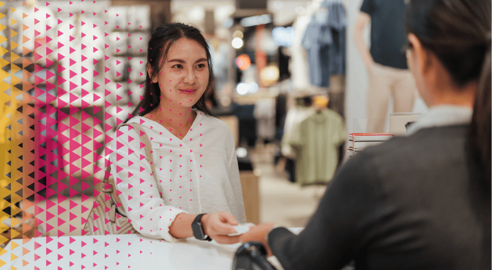 Cliente sonriente entregando una tarjeta de pago a una dependienta en un mostrador con TPV, representando el uso de un software para tiendas y retail moderno en un comercio unificado.